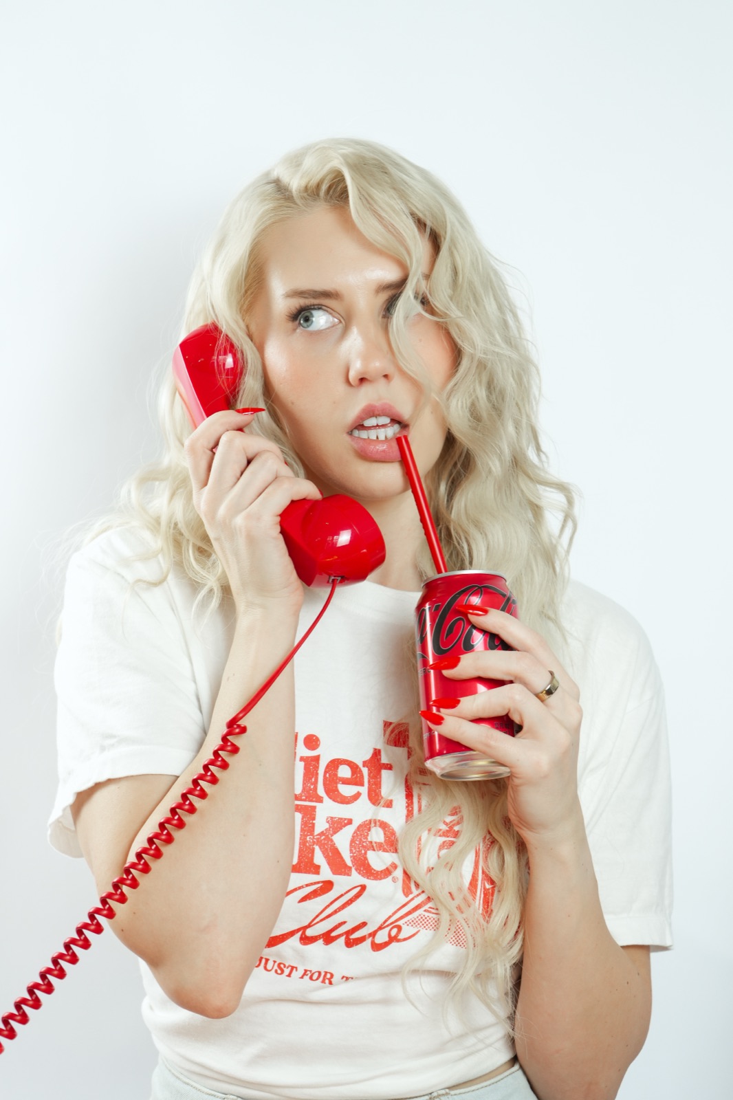 Ida Angelma in a Diet Coke tee on a red telephone, sipping from a can