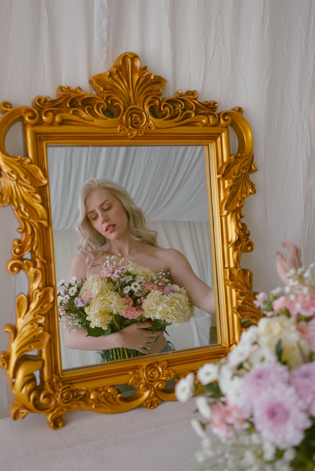 Ida Angelma reflected in a gold mirror holding flowers