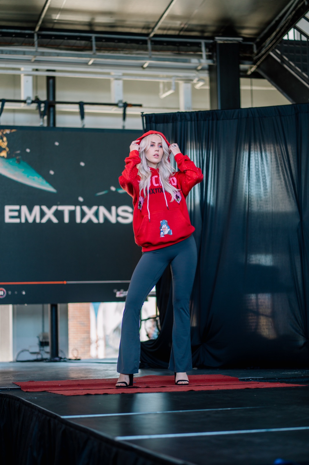 Ida Angelma at the Rebel Wrld Fashion Show in a red hoodie and flared jeans